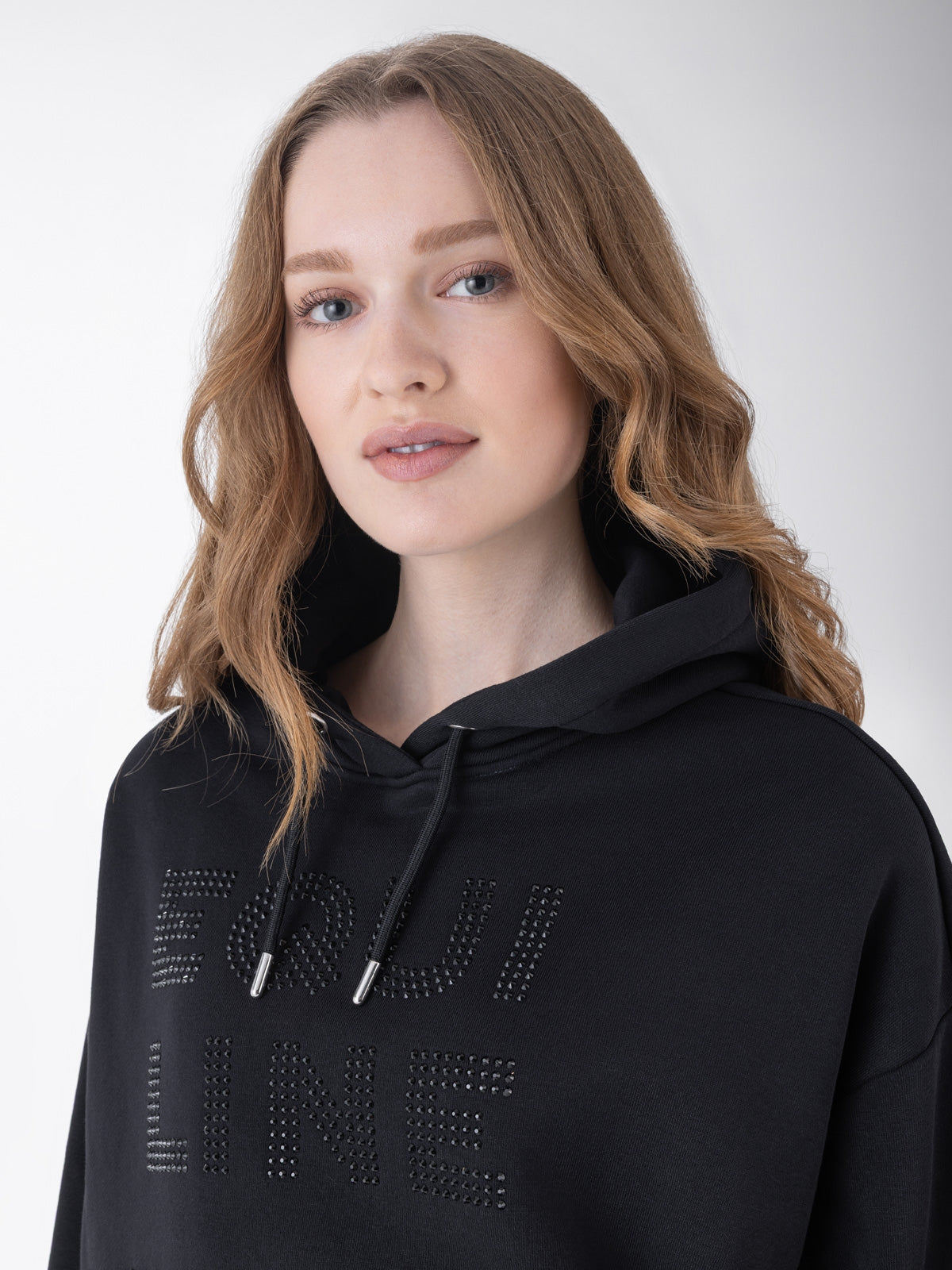 Equiline Ladies Eqglam Oversized Hoodie in Black, detail view of the oversized hoodie with kangaroo pocket and rhinestone Equiline logo.