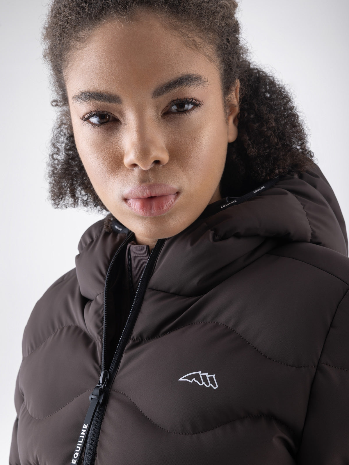 Equiline Ladies Eqcentry Padded Jacket in Coffee Bean, detail view of the hooded Eco-Duvet padded jacket with printed Equiline logo on the chest.